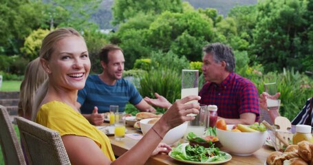 Caucasian woman making a toast turning and smiling during family celebration meal in garden