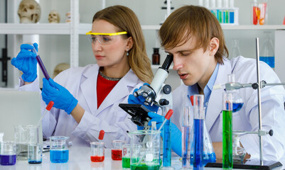 Fototapeta premium Caucasian man and woman scientist in laboratory. Man scientist look through microscope and woman scientist hold and look at test tube and equipment science are many test tube