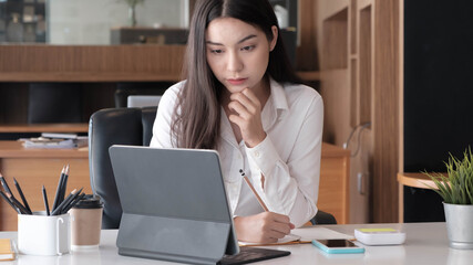 Photo of cheerful joyful asian woman writing down notes holding tablet for data analysis