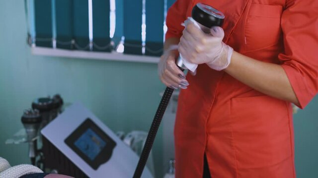 CU shot: female cosmetologist in orange uniform cleans manipulator of massaging equipment disinfecting vibrator in modern cosmetology clinic closeup