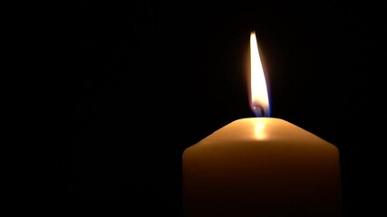 Single big yellow candle flame lights and extinguish in a right corner, isolated on a black background. Slow motion, low angle close up.
