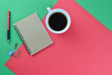 A cup of coffee, notebook and pen over red and green background with copy space