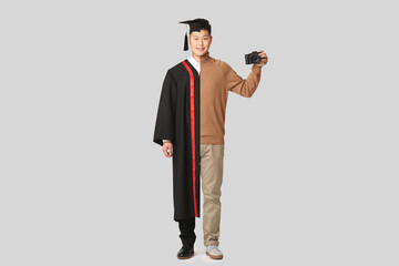 Comparison portrait of young Asian man in bachelor robe and with photo camera on grey background