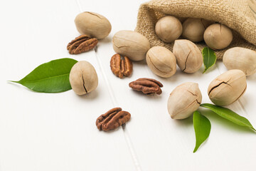 Peeled and unpeeled pecans are spilled out of a bag on a white table.