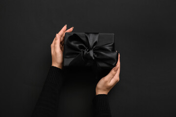 Female hands with gift box on dark background