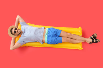 Handsome man lying on inflatable mattress against color background