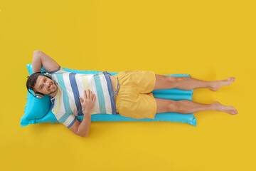 Handsome man listening to music while lying on inflatable mattress against color background