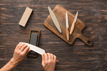 Man sharpening knife on wooden background - obrazy, fototapety, plakaty