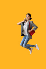 Fototapeta na wymiar Jumping young woman talking by mobile phone on color background