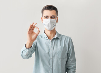 Young man in medical mask showing OK on light background