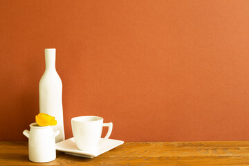 White coffee cup with vase of flower on wooden table. brown background