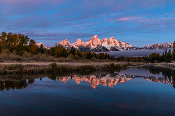 dramatic wintry autumn sunrise of the Grand Tetons mountain range  and its reflection.