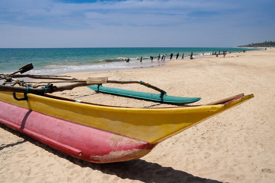 At Ambalangoda, Sri Lanka, a traditional outrigger sea canoe (oru) rests on the sand as fishermen in the background haul in their large net (madela).