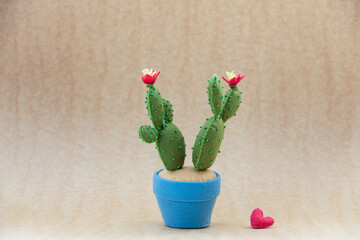 A felt handmade green blooming prickly pear cactus toy with  heart are on a light beige  background. Concept wedding proposal, gift, mother's day, valentine's day.