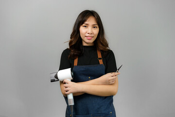 Portrait of Asian gorgeous cheerful young female professional hairdresser holding blowdryer smiling...