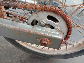 Rusty chain and sprocket for rear wheel of motorcycle on cement flooring closeup. 