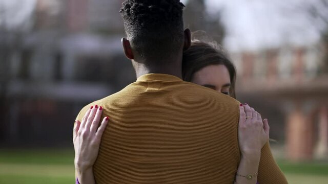 Young interracial couple hugging outside. Empathic embrace standing outside at park