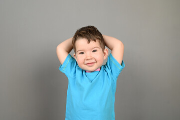A smiling Caucasian boy in a blue T-shirt poses on a gray background.