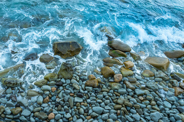 Multicolored round boulders carved by sea waves in the surf and blue sea