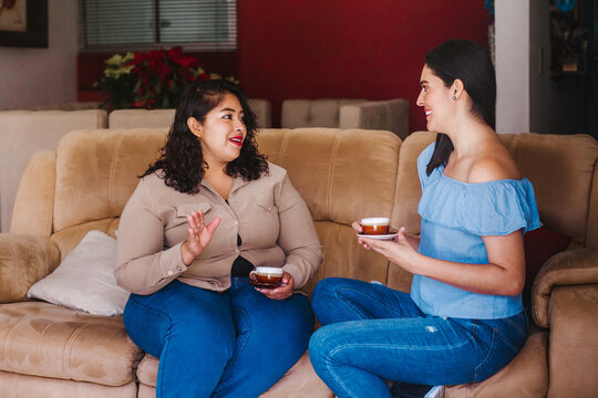 Mexican Friends Women Talking And Drinking Coffee And Tea Sitting On A Couch At Home In Mexico City