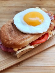 Sandwich with a fried egg, bacon, cheese and vegetables