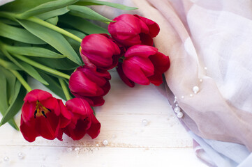 beautiful bouquet of red tulips and a scarf on a light wooden background. spring card, 8 March.
