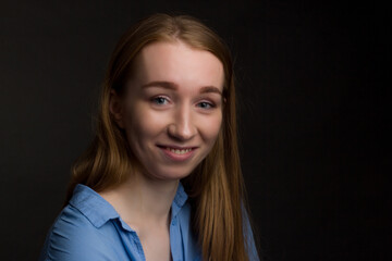 A young woman in a blue blouse, a portrait on a black studio background.