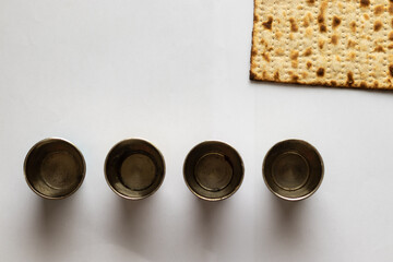 Matzah - Jewish bread for Passover. Next to four silver cups. White background
