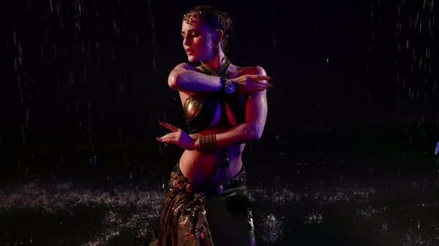 enigmatic shot of pretty belly dancer under rain, woman on her knees in dark