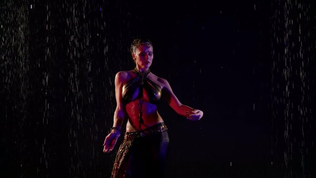 sexy busty woman is dancing belly dance under rain, wriggling her beautiful body with big breasts