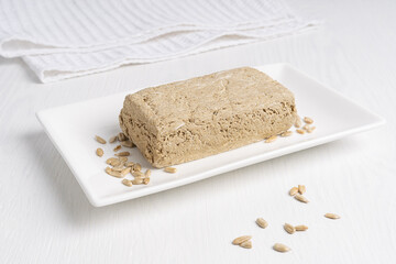 Halva, also halvah or halwa, asian homemade local sweet dessert made of sunflower seeds paste and sugar syrup served in rectangular plate on white wooden background with textile towel. Horizontal