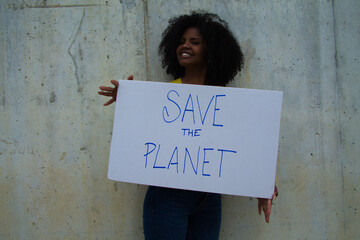 african-american woman with a banner in her hands saying save the planet. In the background grey wall. © @skuder_photographer