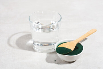 spirulina powder in a spoon on a gray table, glass of water