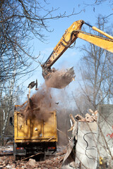 excavator loading a dump truck with debris and trash after building demolition