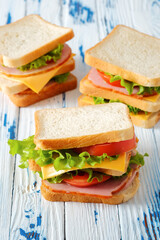 Three tasty sandwiches with ham, salad, cheese and tomatoes on rustic wooden table, selective focus, close-up view, vertical orientation