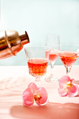 Summer tropical pink cocktail wine champagne in a different glasses decorated pink orchid flowers. Human hand pouring from shaker cocktail