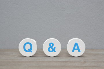 Q and A letter on white circle shape on wooden table over white wall background, Frequently asked...