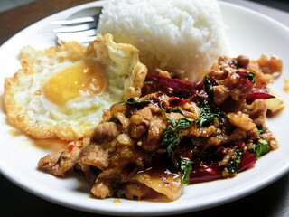 Stir-fried pork and basil and fried egg with steamed rice in a white dish