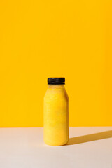 Smoothies of yellow color in a bottle on a yellow background with hard shadows. The concept of sports nutrition.