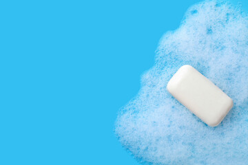 A white bar of soap and soap suds on blue background with copy space.