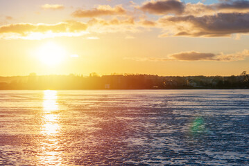 Winter landscape with frozen lake at sunrise or sunset. Lake glistening ice reflect a sun.Forest in the background.