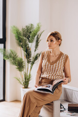 Stylish blonde woman in nude clothes reads a fashion magazine. Soft selective focus, artistic noise.