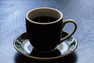 Black ceramic earthenware coffee cup on a saucer on a dark clean table.