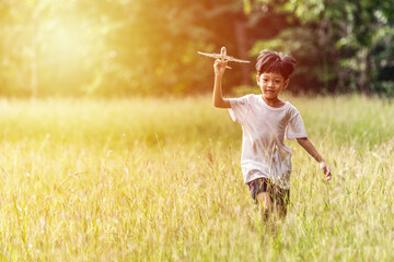 Cute Asian child playing airplane in the park outdoors Happy Asian boy holding a plane runs in a meadow with sunset.