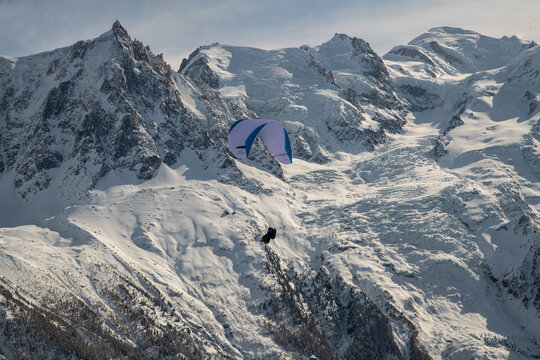 Person Paragliding Over Snow Covered Mountains Against Sky