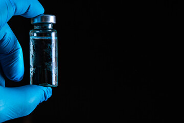 Sars-Kov-2 coronavirus vaccine in a transparent glass ampoule, covered with frost, on a dark background, short focus, toning