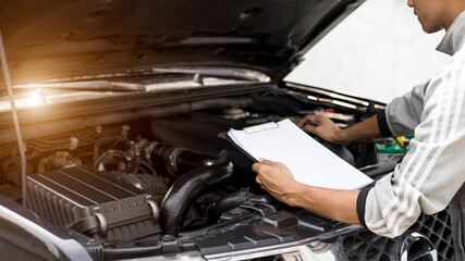 Automobile mechanic repairman checking a car engine with inspecting writing to the clipboard the...