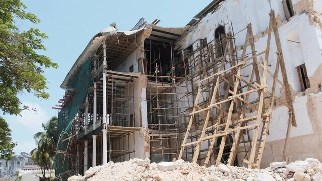 Collapsed building of the House of Wonders in Stone Town, Zanzibar, Africa. African builders reconstruct crumbling building. High-rise builders work in makeshift log scaffolding without belay.