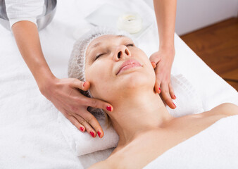 Fototapeta na wymiar Aged smiling woman having professional face massage in spa salon