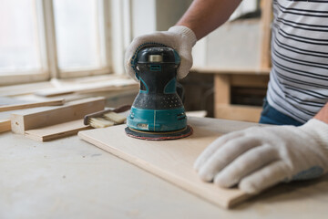 Сarpenter working with wood using electric sander from workshop. Joinery work on the production and renovation of wooden furniture. Small Business Concept. Close up